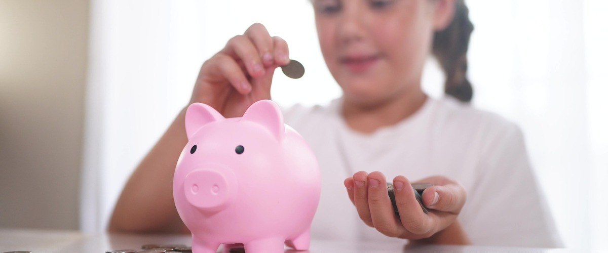 Bild zeigt ein Kind mit einem rosa Sparschwein verlinkt auf Blogbeitrag Berufsunfähigkeitsversicherung für Kinder