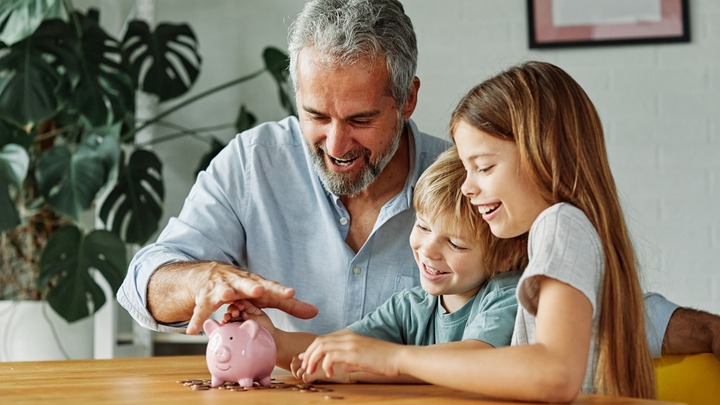 Großvater sitzt mit Enkeln vor einem Sparschwein